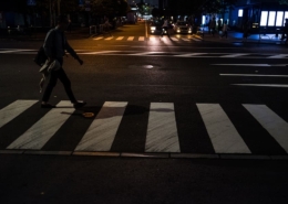 Pedestrian crossing a marked crosswalk at dusk with car headlights approaching