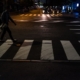 Pedestrian crossing a marked crosswalk at dusk with car headlights approaching